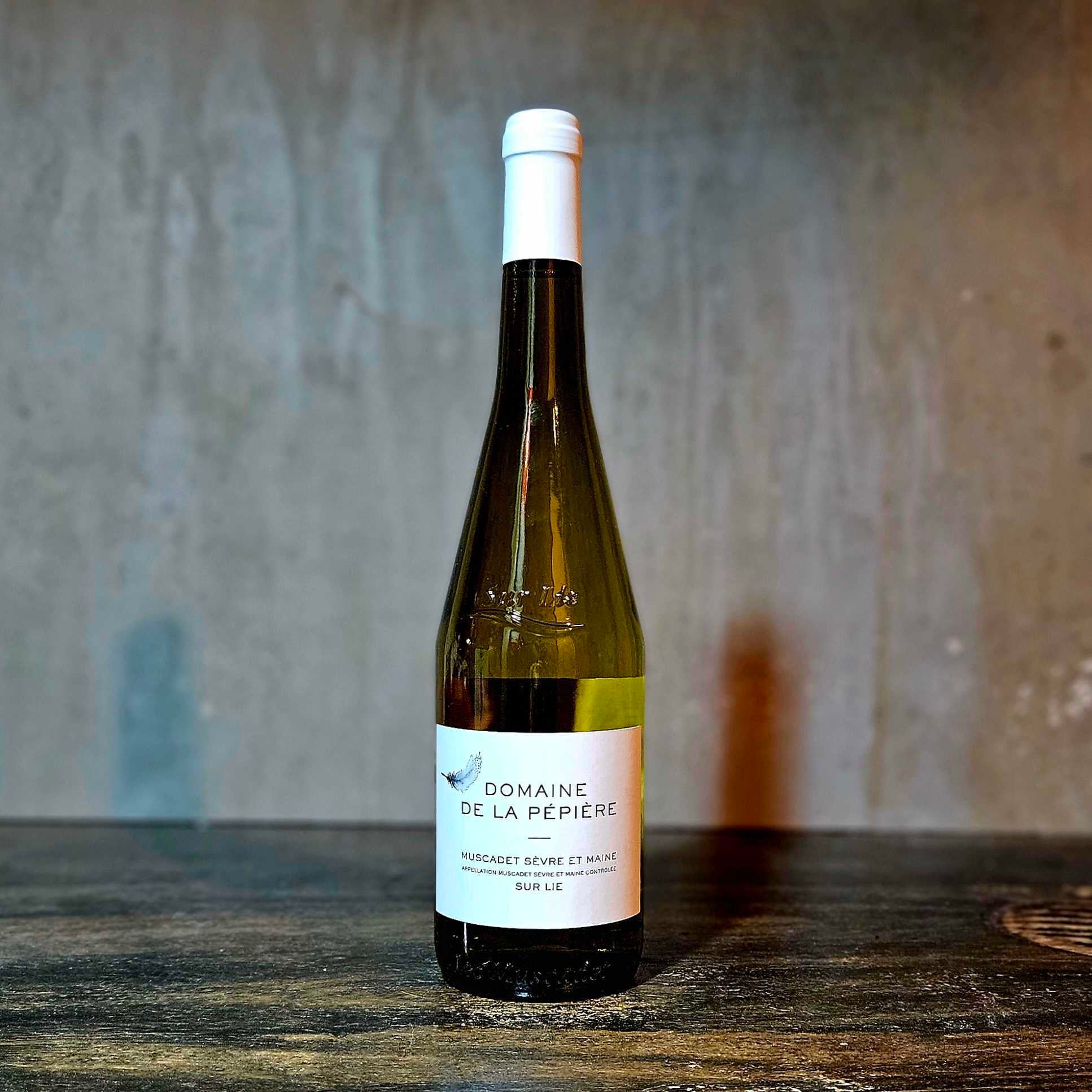 A bottle of Domaine La Pepiere Muscadet wine with a white label, placed against a concrete background.
