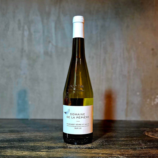 A bottle of Domaine La Pepiere Muscadet wine with a white label, placed against a concrete background.