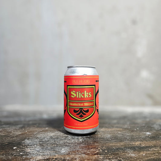 Beer can with 'Sticks' label on a wooden surface and gray background